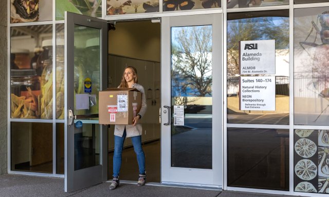 Photo of person holding a box in front of the biorepository at ASU