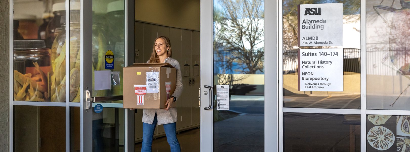 Photo of person holding a box in front of the biorepository at ASU