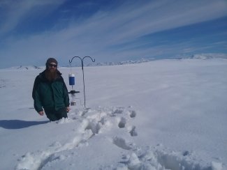 Field technician standing in snow next to a carbon dioxide light trap. 