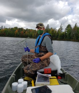 Domain 05 field ecologist prepares to collect aquatic plants at the CRAM lake field site using a rake 