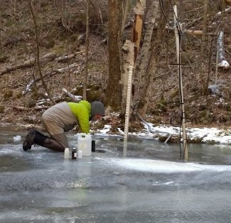 Ryan Williams collects water through the ice after using a heavy iron ice breaker. 