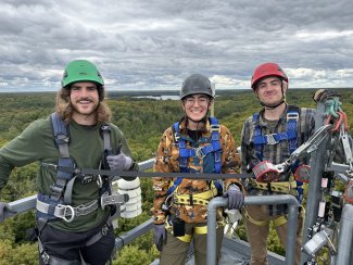 Three field technicians standing at the top of a flux measurement tower at the University of Notre Dame Environmental Research Center field site. 