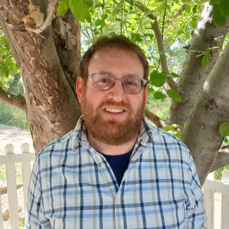 Keith Krause smiling and looking at the camera outside in front of a tree