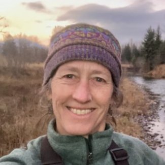 Christa Torrens outside wearing a winter hat and smiling at camera with a river behind her.
