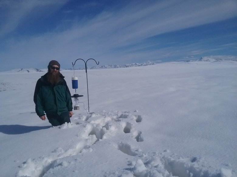 Field technician standing in snow next to a carbon dioxide light trap.